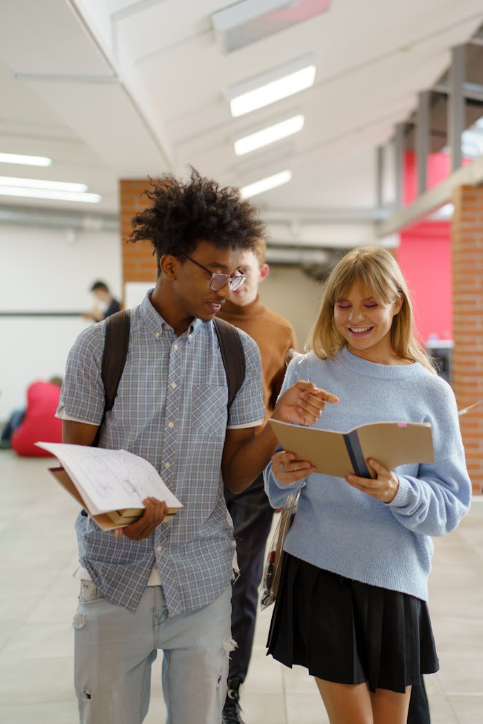 services-04 Cheerful students discuss in a university hallway, engaging with notebooks and learning materials.