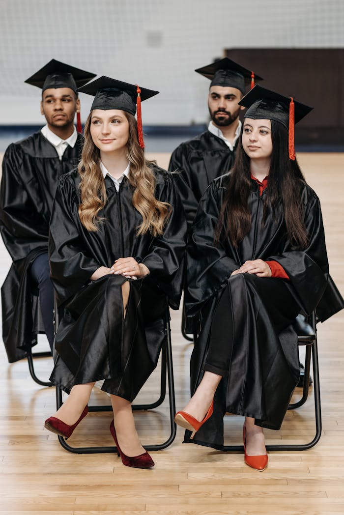 A group of graduates in caps and gowns sitting indoors at a graduation ceremony, celebrating their achievement.