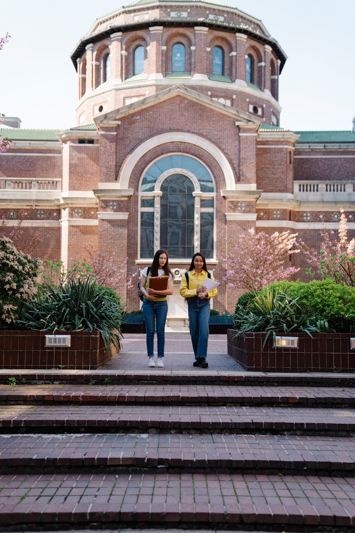 services-03 Two young women walking past a historic university building on a sunny day.